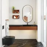 Modern and stylish bathroom inspiration with an oval mirror with a black frame and light control, colored toilet, vanity unit, base cabinets, and cabinets in reddish-brown oak, Silestone sink and matching floor