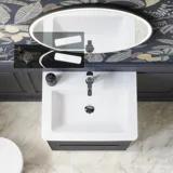 Bathroom inspiration with dark blue wall panels, romantic floral wallpaper, dark blue vanity with soft curves, and a beautiful round mirror with light, creating a vintage look