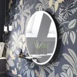 Bathroom inspiration with dark blue wall panels, romantic floral wallpaper, dark blue vanity with soft curves, and a beautiful round mirror with light, creating a vintage look