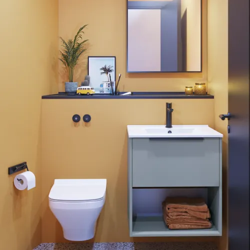 Small bathroom inspiration with slanted and warm yellow walls, elegant light blue vanity unit, thin and sleek sink, and minimalist square mirror with a black edge and practical lamp.