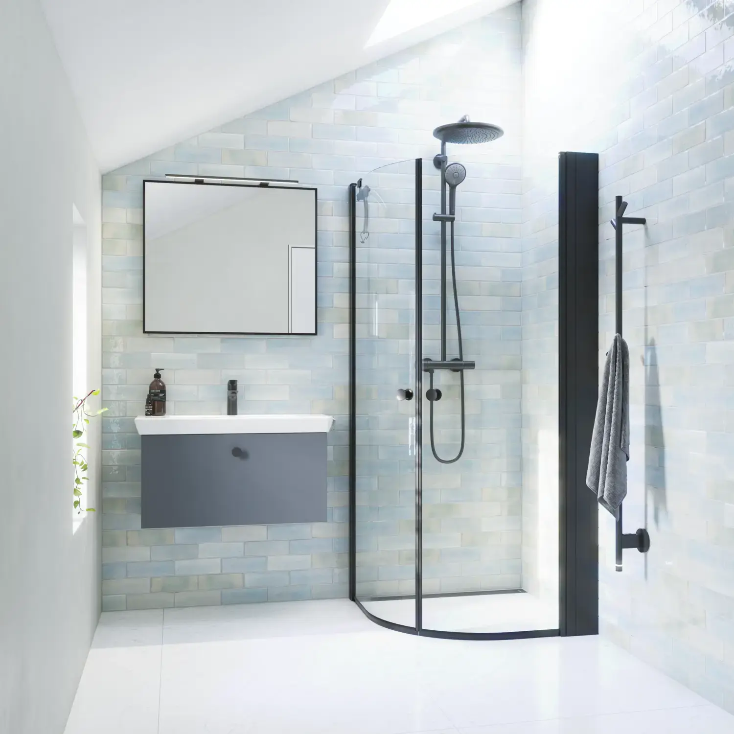 Bathroom inspiration with gray vanity unit with square mirror with black edge and lamp, rounded shower doors in clear glass and profiles in black matt, with electric towel dryer and bathroom shelf.
