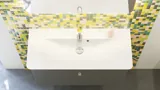 Bathroom inspiration with bathroom furniture in matt grey with elegant washbasin, beautiful square mirror, grey floor and small tiles in different shades of yellow and green, which with yellow wall gives a bright and playful expression