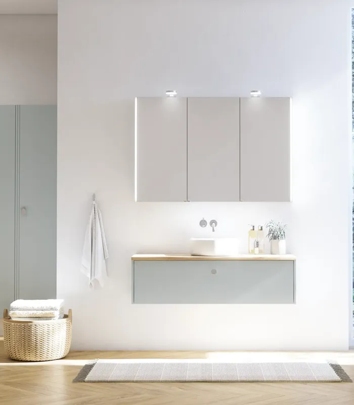 Large bathroom inspiration in Nordic style with bathroom furniture in light blue colour and wooden countertop with elegant countertop basin, herringbone wooden floor creating a bright and classic style